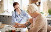 Nurse checking elderly woman's blood pressure in a bright kitchen setting