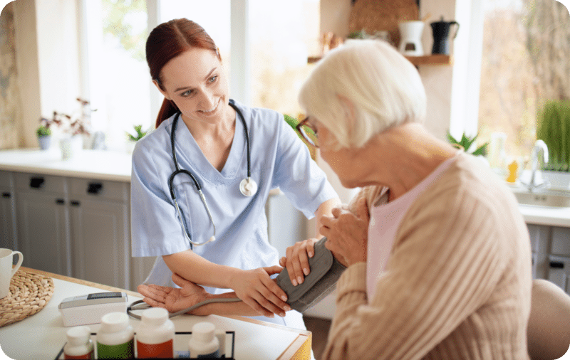 Nurse checking elderly woman's blood pressure in a bright kitchen setting