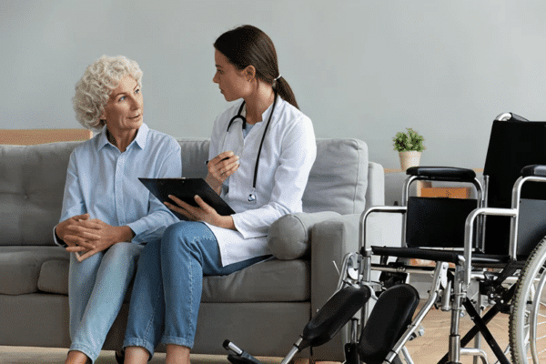 Elderly woman consulting with female doctor at home next to wheelchair