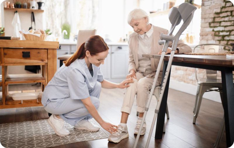 Caregiver assisting elderly woman with crutches at home