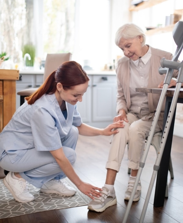 Caregiver assisting elderly woman with crutches in a cozy kitchen setting