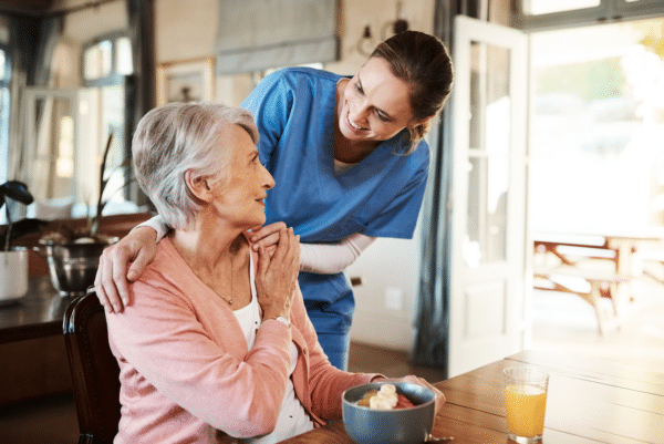 Nurse caring for elderly woman during breakfast at home, showing compassion and support